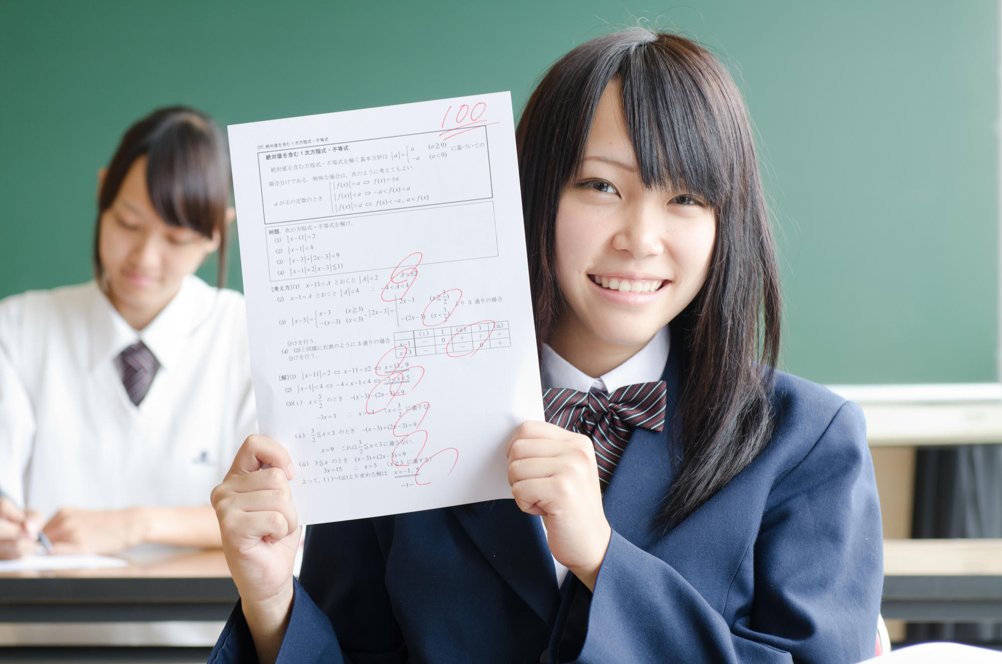 【414-1083J】テスト用紙を掲げる女子学生1.jpg